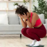 woman crouched down on scales looking upset