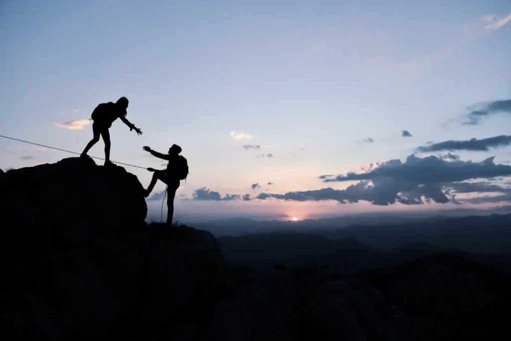 one person reaching down to help another person climb the mountain