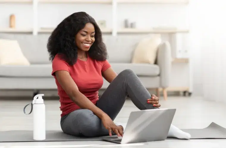 best online weight loss coach: picture of a woman sat on the floor smiling at a laptop.