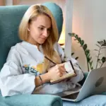 health coaching for weight loss: Woman sat in an armchair making notes while working at a laptop.