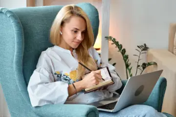 health coaching for weight loss: Woman sat in an armchair making notes while working at a laptop.