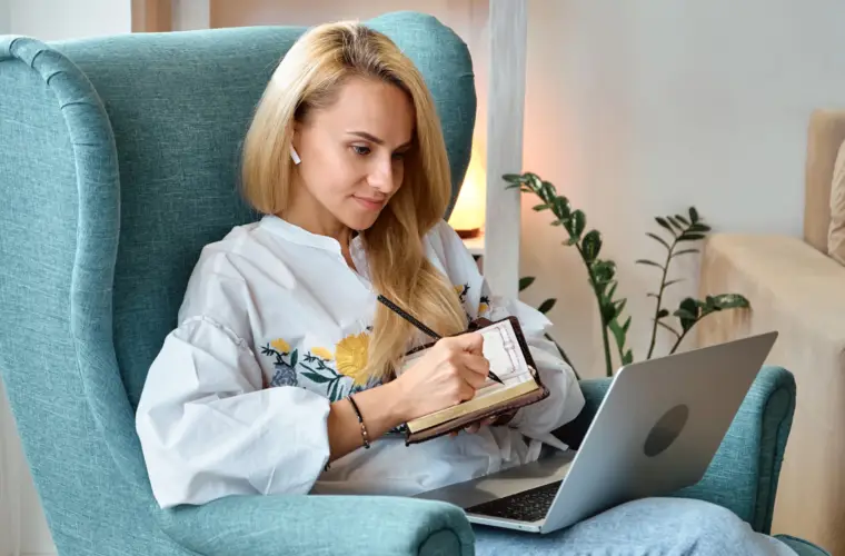 health coaching for weight loss: Woman sat in an armchair making notes while working at a laptop.